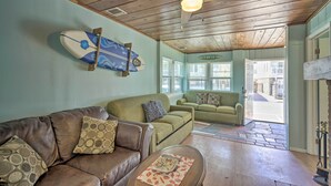 A cozy living room with a brown leather couch, a green armchair, and a wooden coffee table. A ceiling fan and a surfboard decoration are visible. - Inviting Seaside Heights Apt < 1 Mi to Beach! (Seaside Heights)