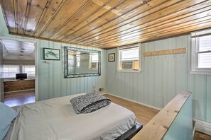 Um quarto com teto de madeira, uma cama com travesseiro estampado, um espelho grande e um aviso na parede.