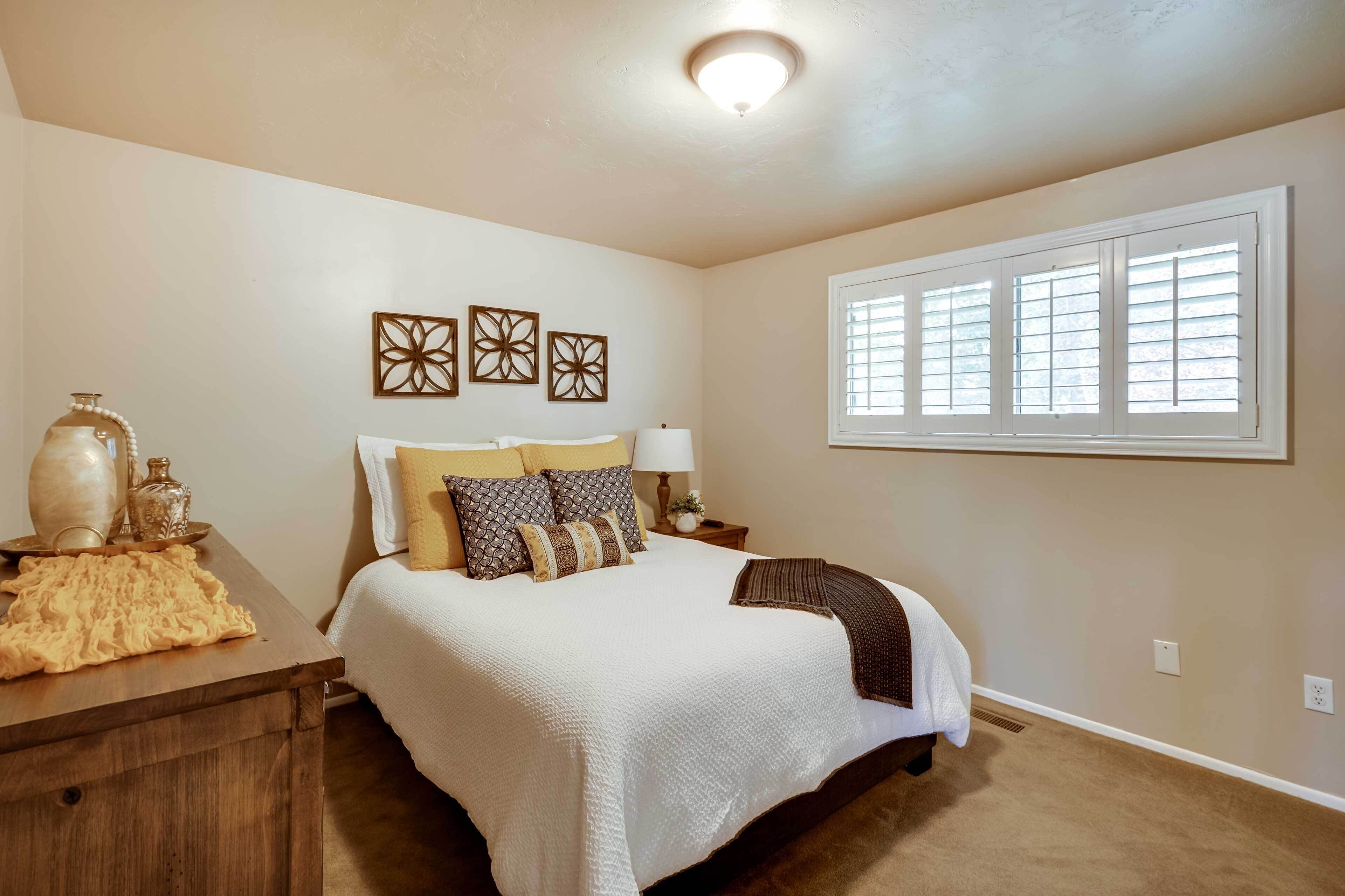 Un dormitorio con una cama grande, una mesita de noche, una lámpara, decoración en la pared y una ventana con persianas.