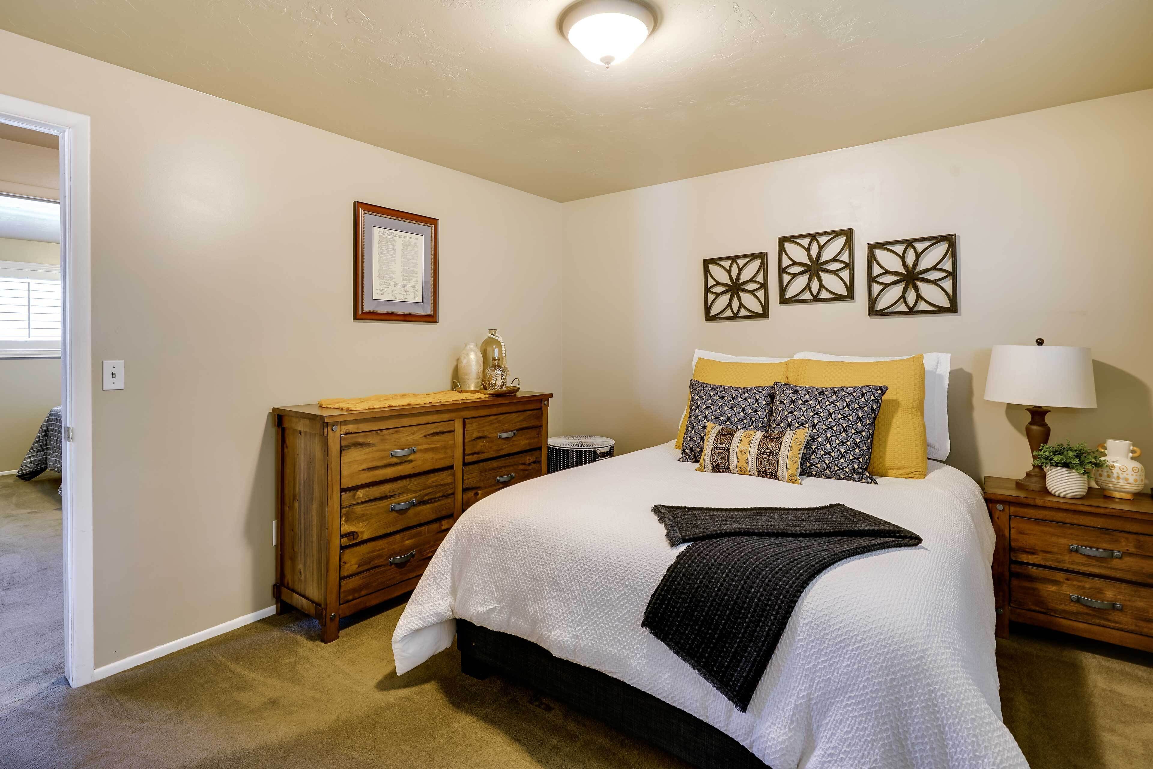 A bedroom with a large bed, wooden dresser, and a nightstand with a lamp.