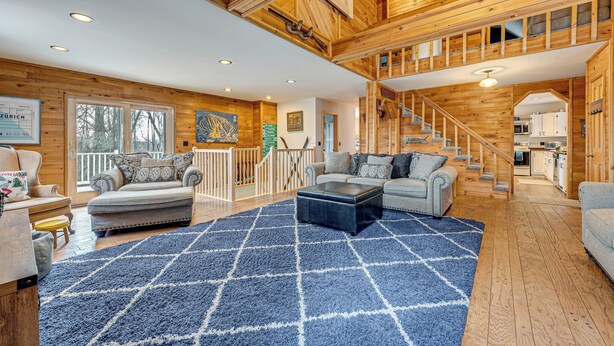 Un vaste espace de vie doté d’un haut plafond, de poutres apparentes et d’un escalier menant à un niveau supérieur.