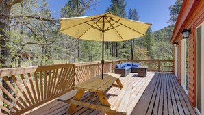 Een houten terras met een picknicktafel en een gele parasol, omgeven door houten leuningen en uitzicht op bomen.