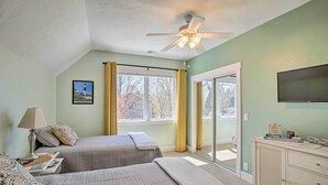 Quarto com duas camas, ventilador de teto, televisão e janela com cortinas.