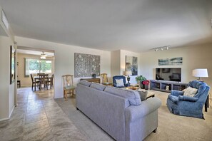 Un salon spacieux avec un canapé d’angle gris, un fauteuil bleu et un meuble pour la télévision équipé d’un écran plat.
