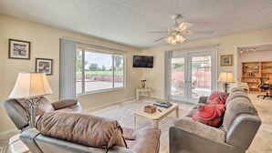 A spacious living room with a ceiling fan, a television, and a large window. - Quiet Sun City Home w/ Grill - Golf & Hike Nearby! (Sun City)