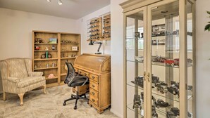A room with a wooden desk, a chair, a bookshelf, and a glass display case with model cars. - Quiet Sun City Home w/ Grill - Golf & Hike Nearby! (Sun City)