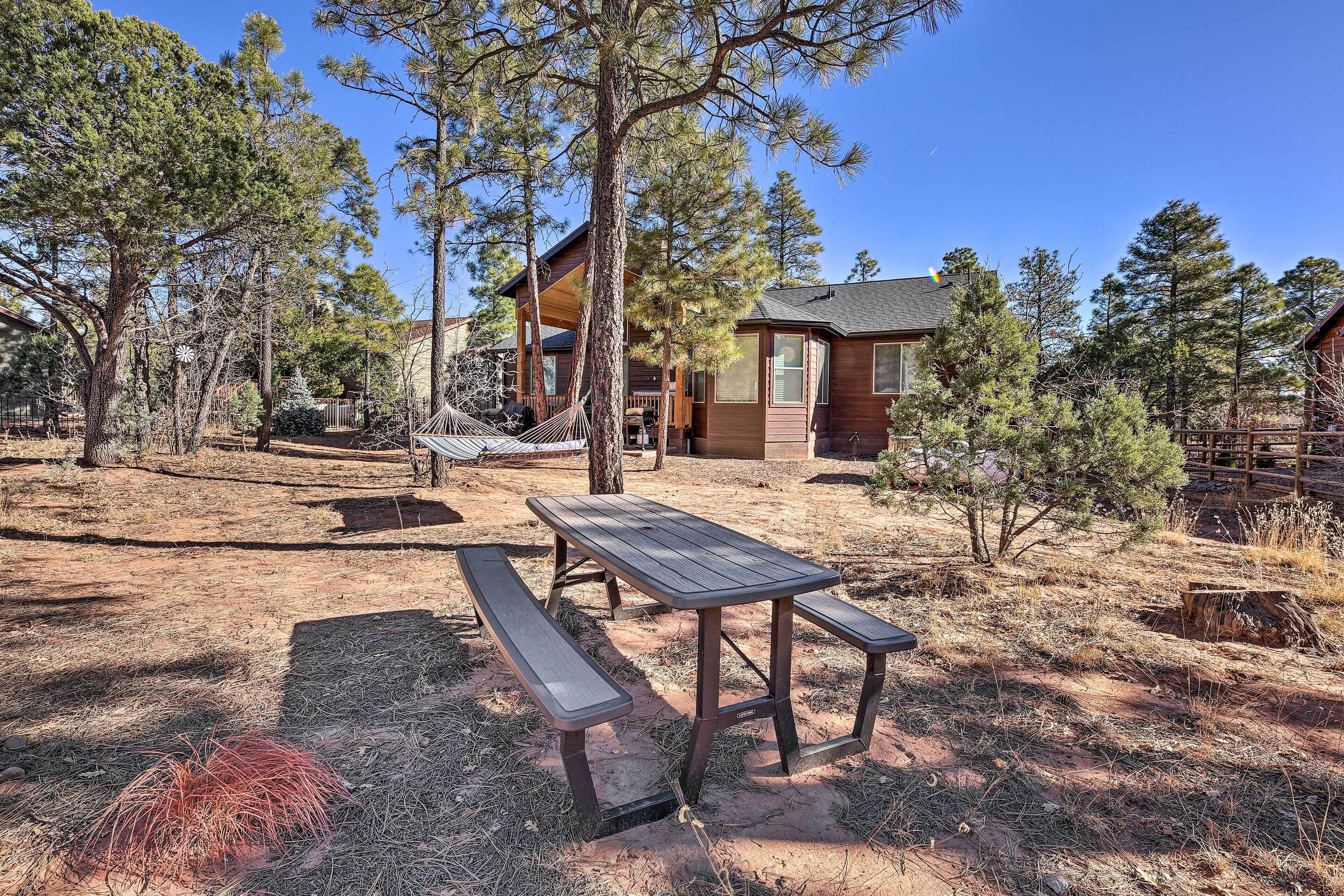 A wooden picnic table with benches in a forested area with cabins.