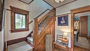 A staircase with wooden railings, a radiator, a chair, and a framed picture of a sailboat. - Luxe Lake Geneva Retreat in Downtown! (Lake Geneva)
