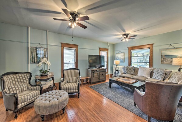 A living room with a sofa, armchairs, ottoman, TV, and ceiling fans.