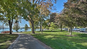 A paved walkway along a grassy area with trees and a view of the water. - Luxe Lake Geneva Retreat in Downtown! (Lake Geneva)