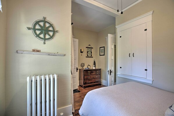 A bedroom with a large bed, a dresser, a radiator, a wall-mounted compass, and a door leading to another room. - Luxe Lake Geneva Retreat in Downtown! (Lake Geneva)