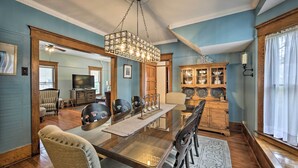 A dining area with a glass-top table, wooden chairs, a chandelier, and a wooden cabinet with glass doors. - Luxe Lake Geneva Retreat in Downtown! (Lake Geneva)