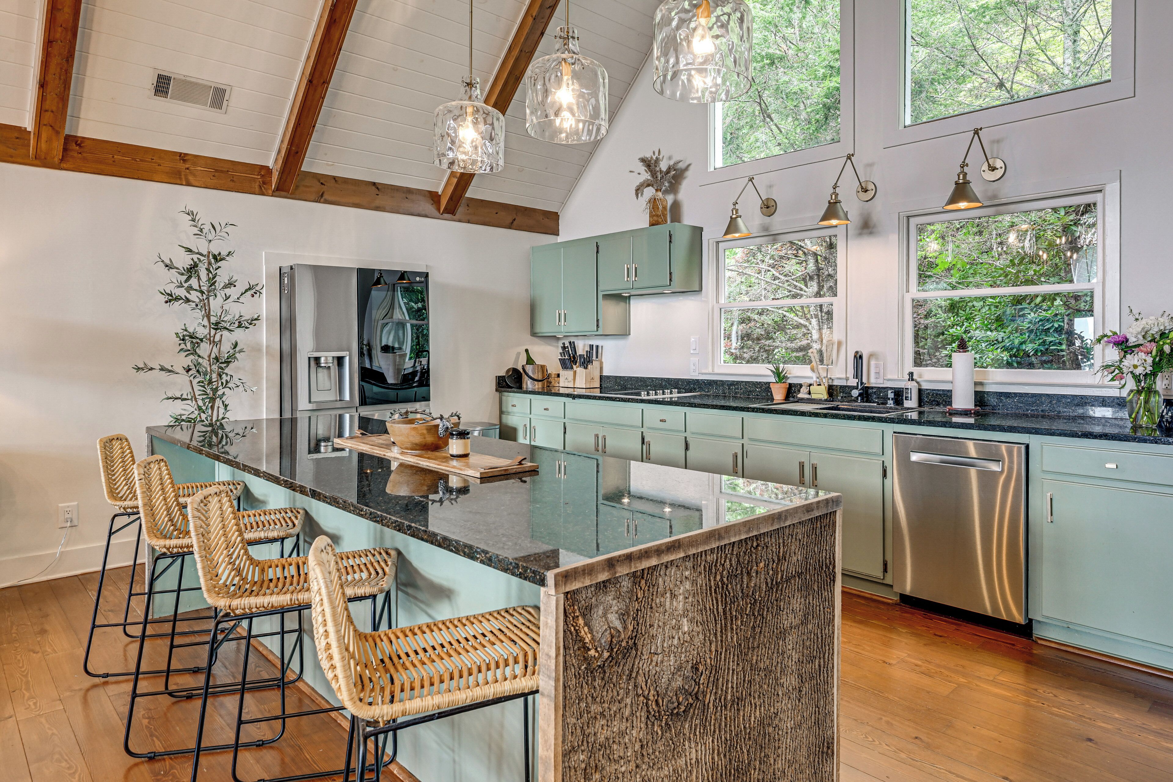 A modern kitchen with a central island, bar stools, and a view of the outdoors through large windows.