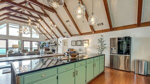 Cucina spaziosa con isola centrale ampia, mobili verdi, elettrodomestici in acciaio inossidabile e soffitto alto con travi in legno.