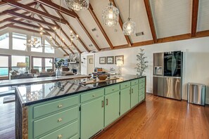 Une cuisine spacieuse dotée d’un grand îlot central, de meubles de couleur verte, d’appareils électroménagers en acier inoxydable et d’un plafond haut avec des poutres en bois.