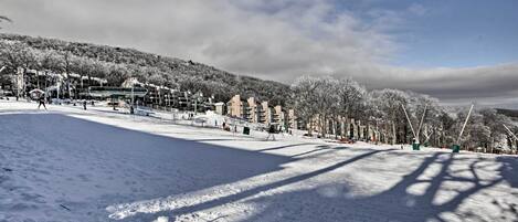 A snow-covered ski slope with buildings in the background and a clear sky.