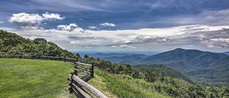 A wooden fence along a grassy path with a view of distant mountains and a partly cloudy sky.