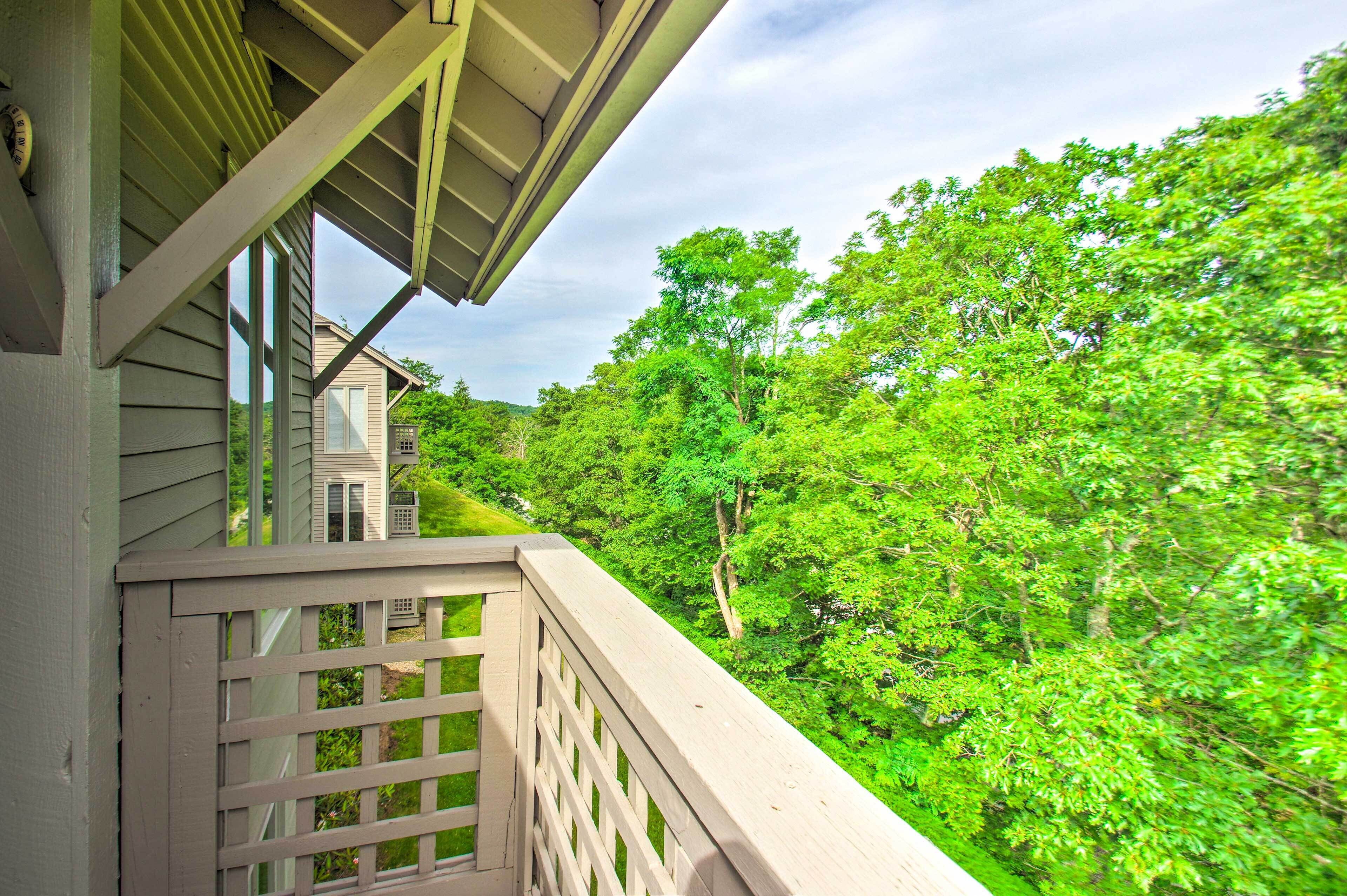 A wooden balcony with a view of a house and lush green trees.