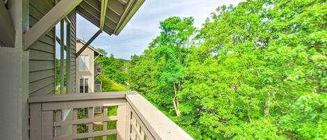 A wooden balcony with a view of a house and lush green trees.