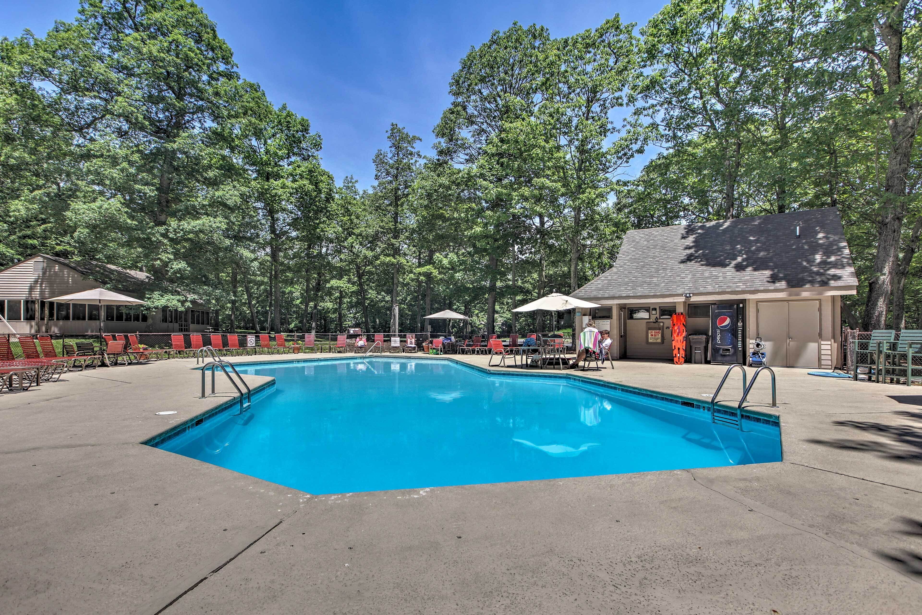 A rectangular swimming pool with a concrete deck, surrounded by red and green lounge chairs, and shaded by umbrellas.