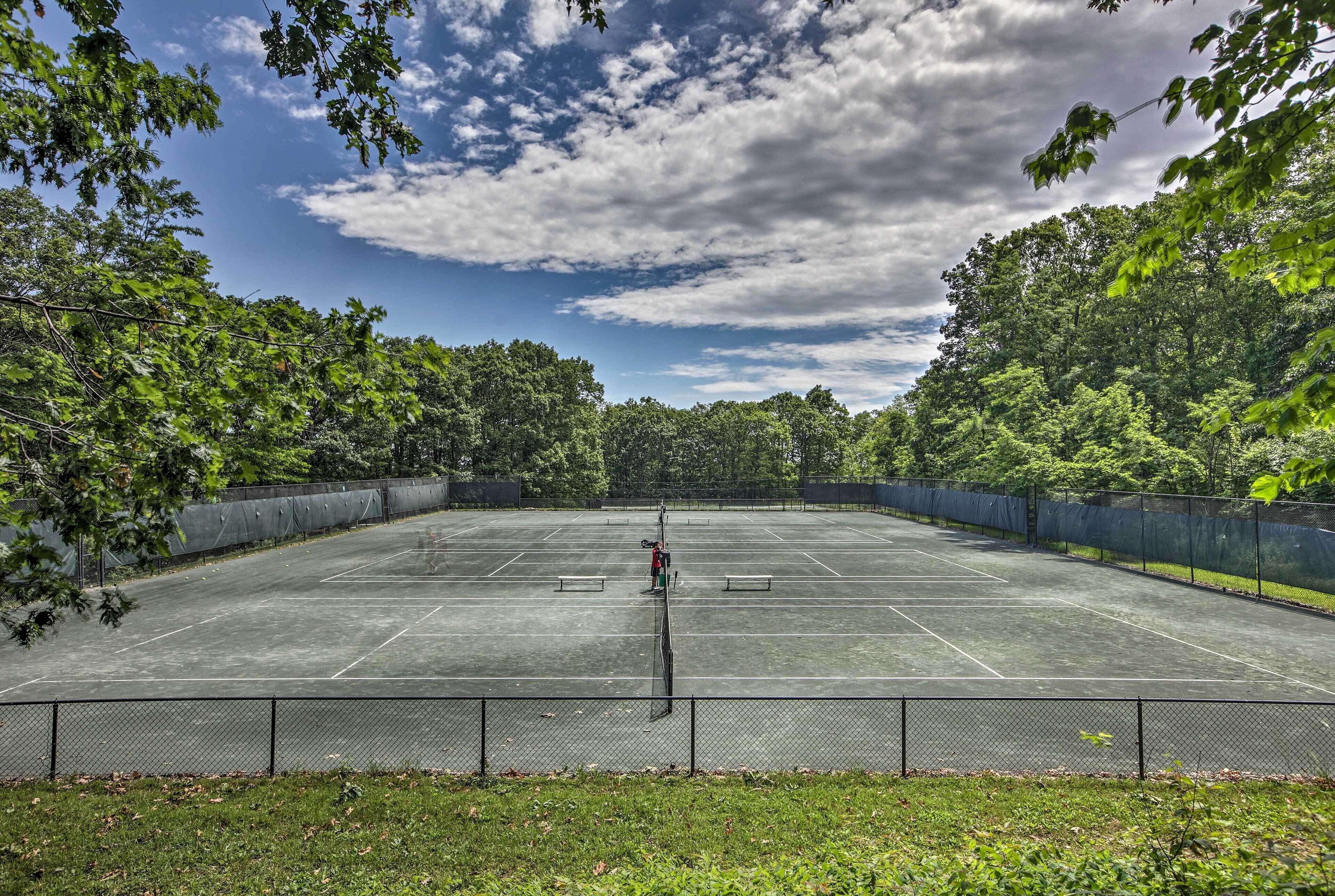 An outdoor tennis court surrounded by trees and a clear sky.