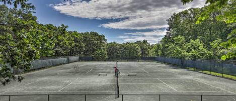 An outdoor tennis court surrounded by trees and a clear sky.