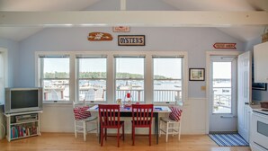 A dining area with a view of a harbor, a television, and a bookshelf.