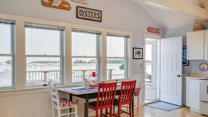 A dining area with a table and chairs, large windows with a view of boats, and a sign that reads "OYSTERS".