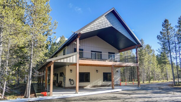 Une maison à deux étages avec un balcon, entourée d’arbres.