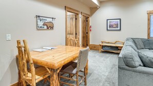 Une table à manger en bois avec des chaises, un canapé gris et un panneau d’accueil encadré.