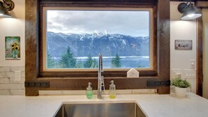 A kitchen with a large window overlooking mountains, a stainless steel sink, and a wooden frame. - Dazzling Cle Elum Home; Mountain Views (Cle Elum)