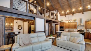 A spacious living area with two white leather sofas, a wooden ceiling, and a kitchen in the background. - Dazzling Cle Elum Home; Mountain Views (Cle Elum)