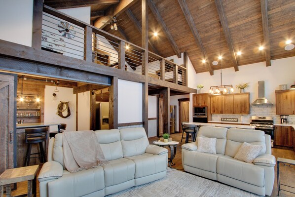 A spacious living area with two white leather sofas, a wooden ceiling, and a kitchen in the background. - Dazzling Cle Elum Home; Mountain Views (Cle Elum)