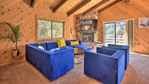 A cozy cabin interior with a stone fireplace, blue upholstered seating, and large windows. - Luxe Escape w/ Decks, Mtn Views, Game Room! (Pine Mountain Club)