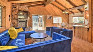 A cozy cabin interior with a stone fireplace, wooden beams, and a blue upholstered sofa. - Luxe Escape w/ Decks, Mtn Views, Game Room! (Pine Mountain Club)