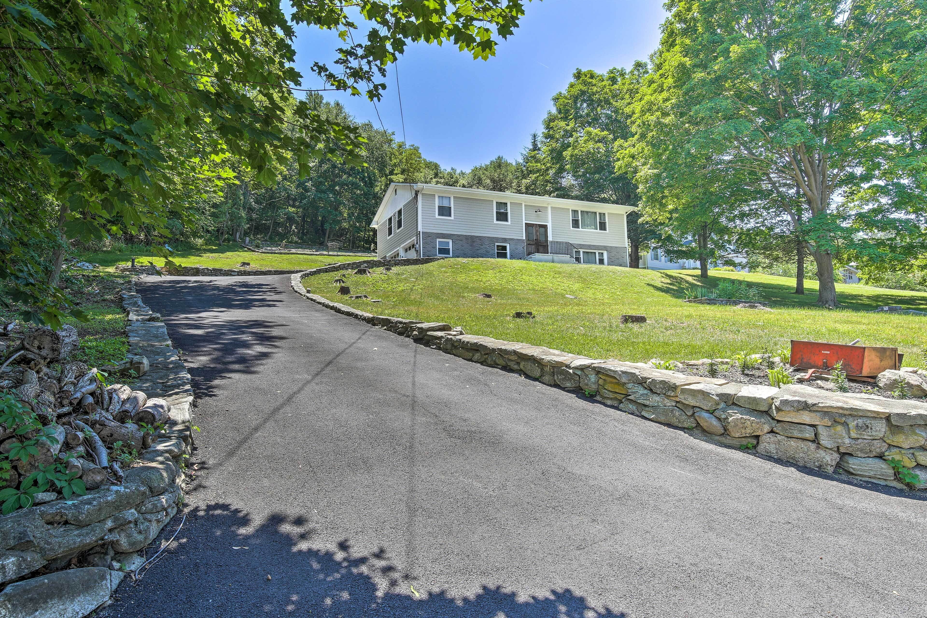 A two-story house with a stone retaining wall and a paved driveway.