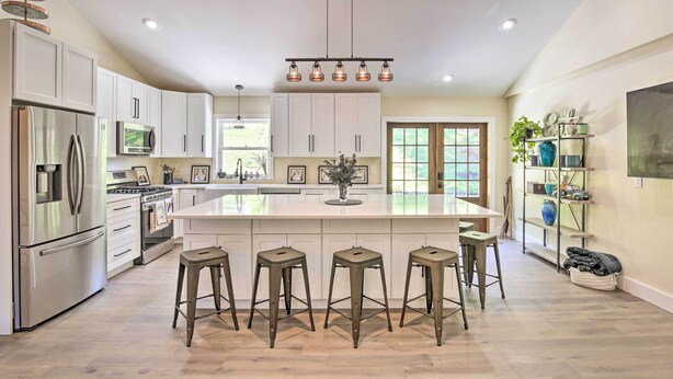 A modern kitchen with white cabinets, stainless steel appliances, a central island with stools, and recessed lighting.