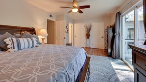 Quarto com cama grande, ventilador de teto, janela com cortinas e vista para o exterior.