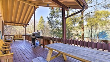 Una terraza de madera con mesa de picnic, parrilla y asientos exteriores.