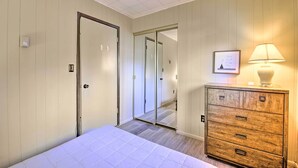 A hotel room with a bed, a wooden dresser, a mirror, and a door leading to another room.