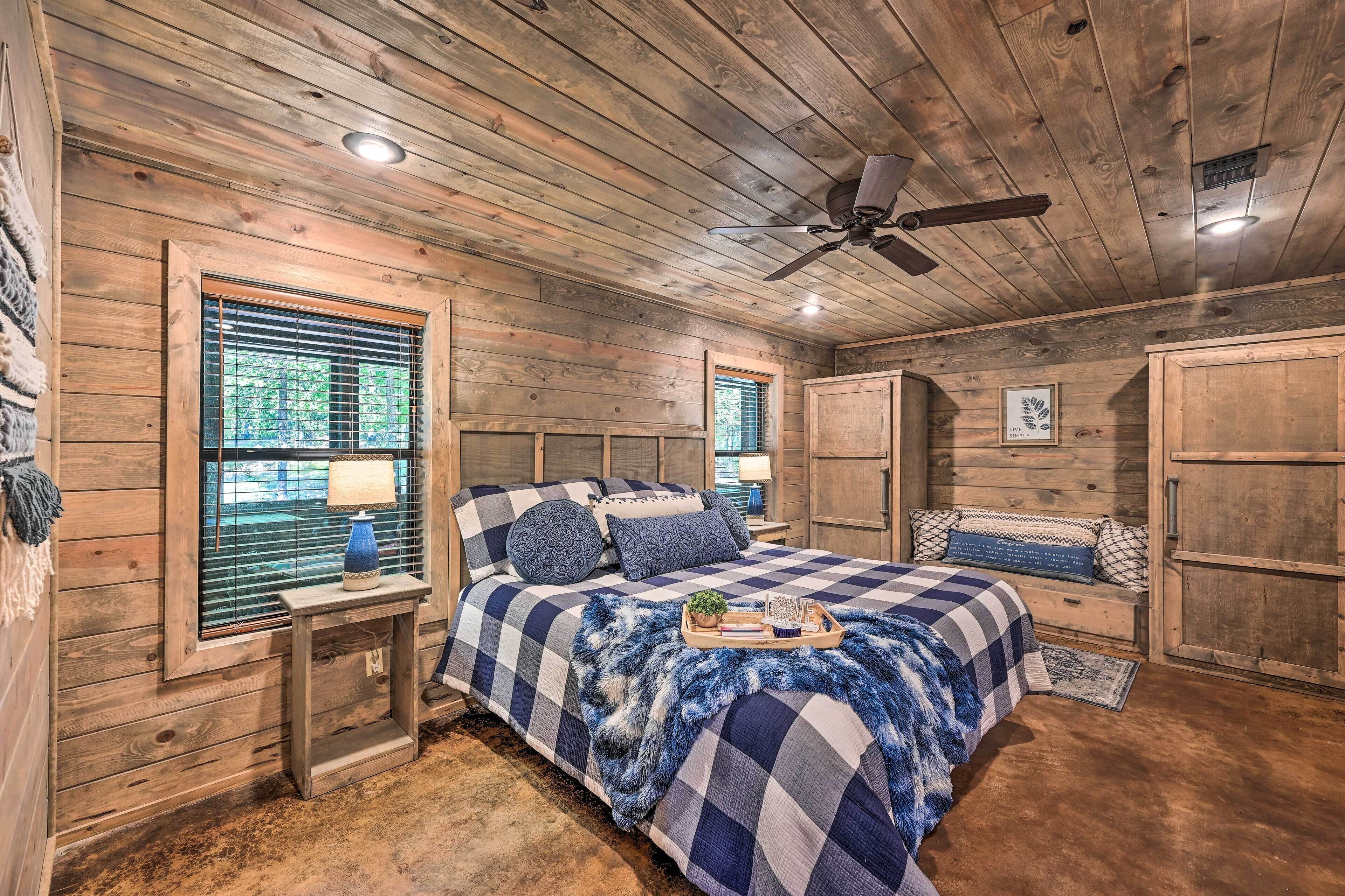 A bedroom with a large bed, wooden walls, a ceiling fan, and a window with blinds.