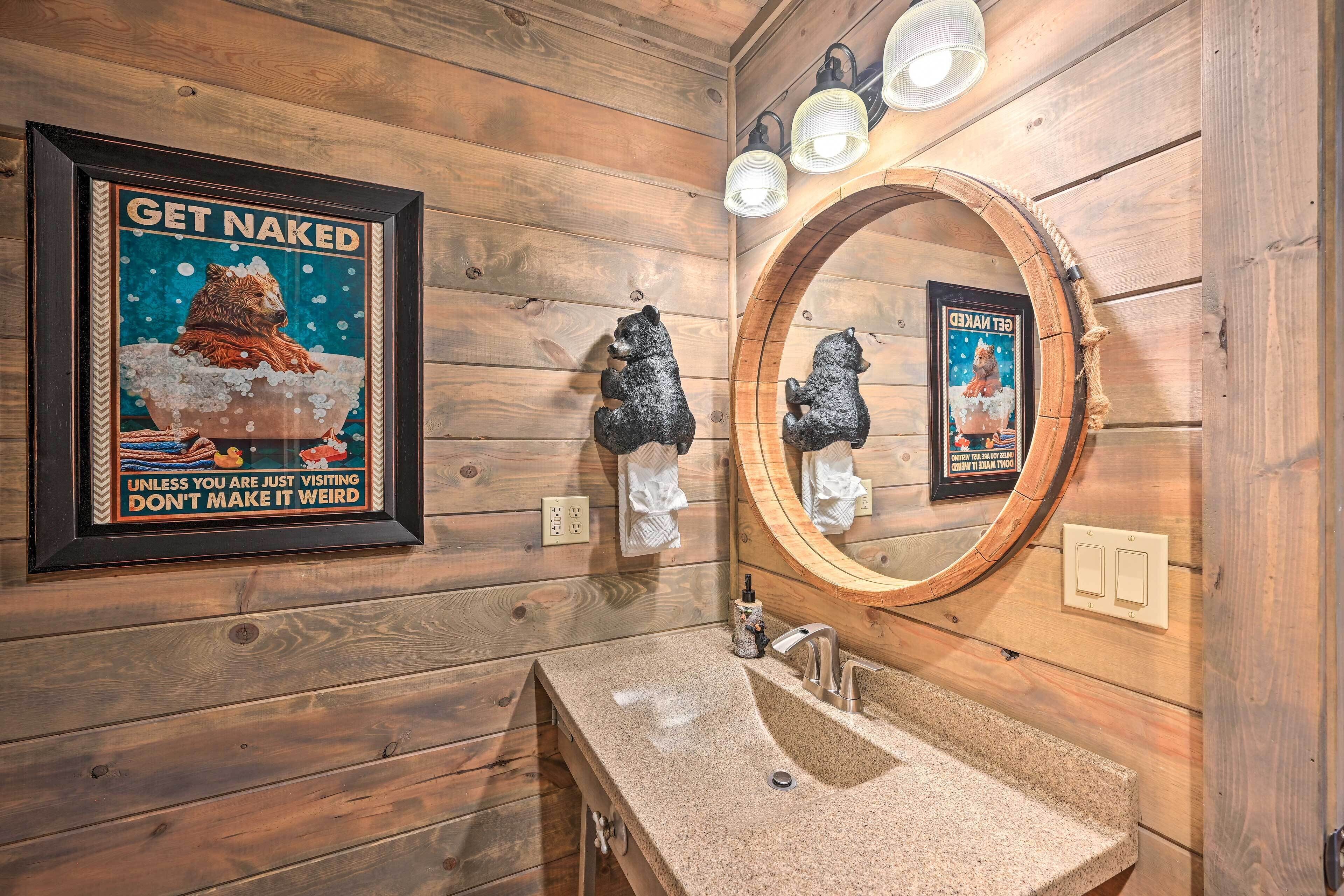Ein Badezimmer einer Holzhütte mit einem gerahmten Poster, einem runden Spiegel und einem Waschbecken.
