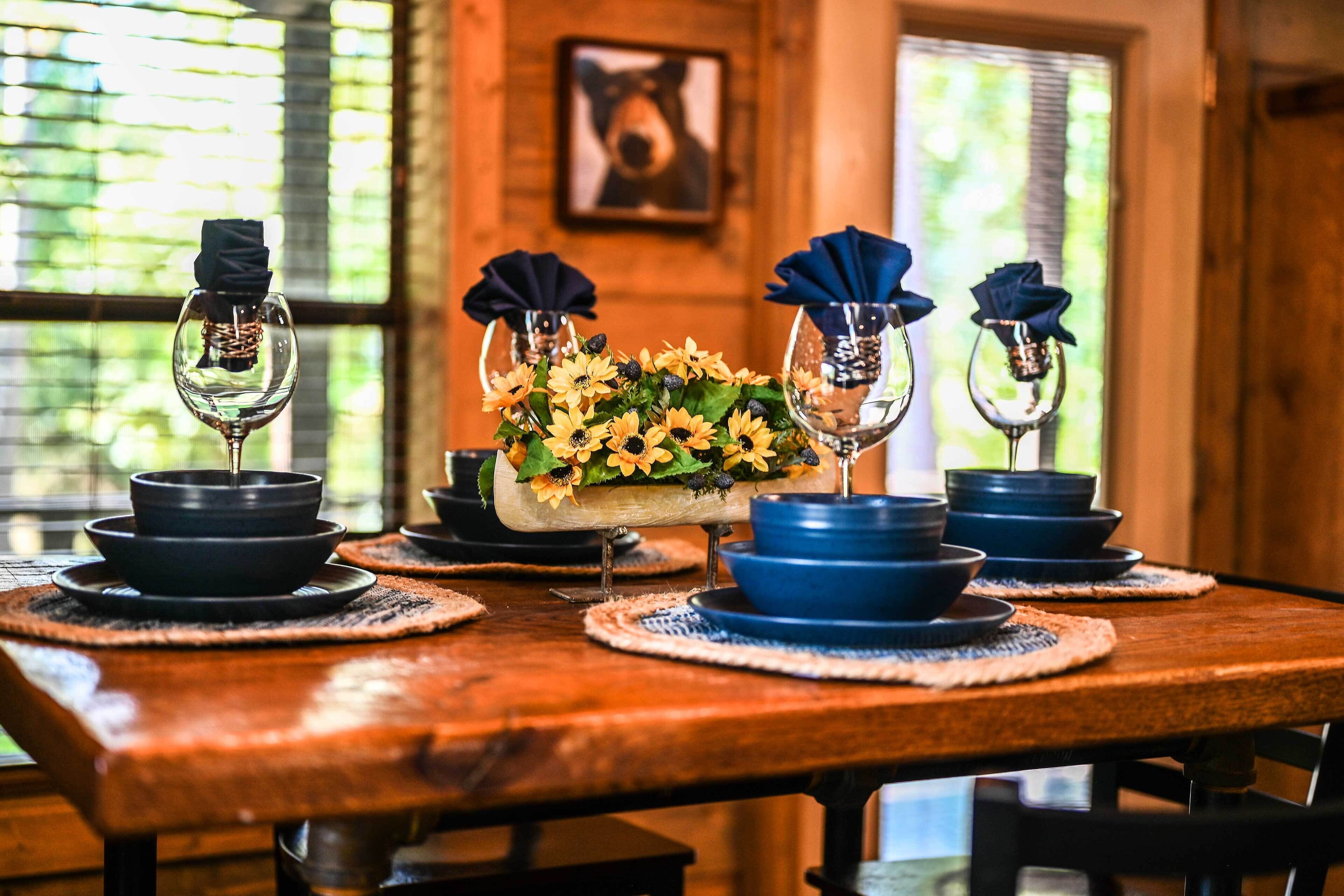 A wooden dining table with blue and black plates, glasses, and a centerpiece of sunflowers.