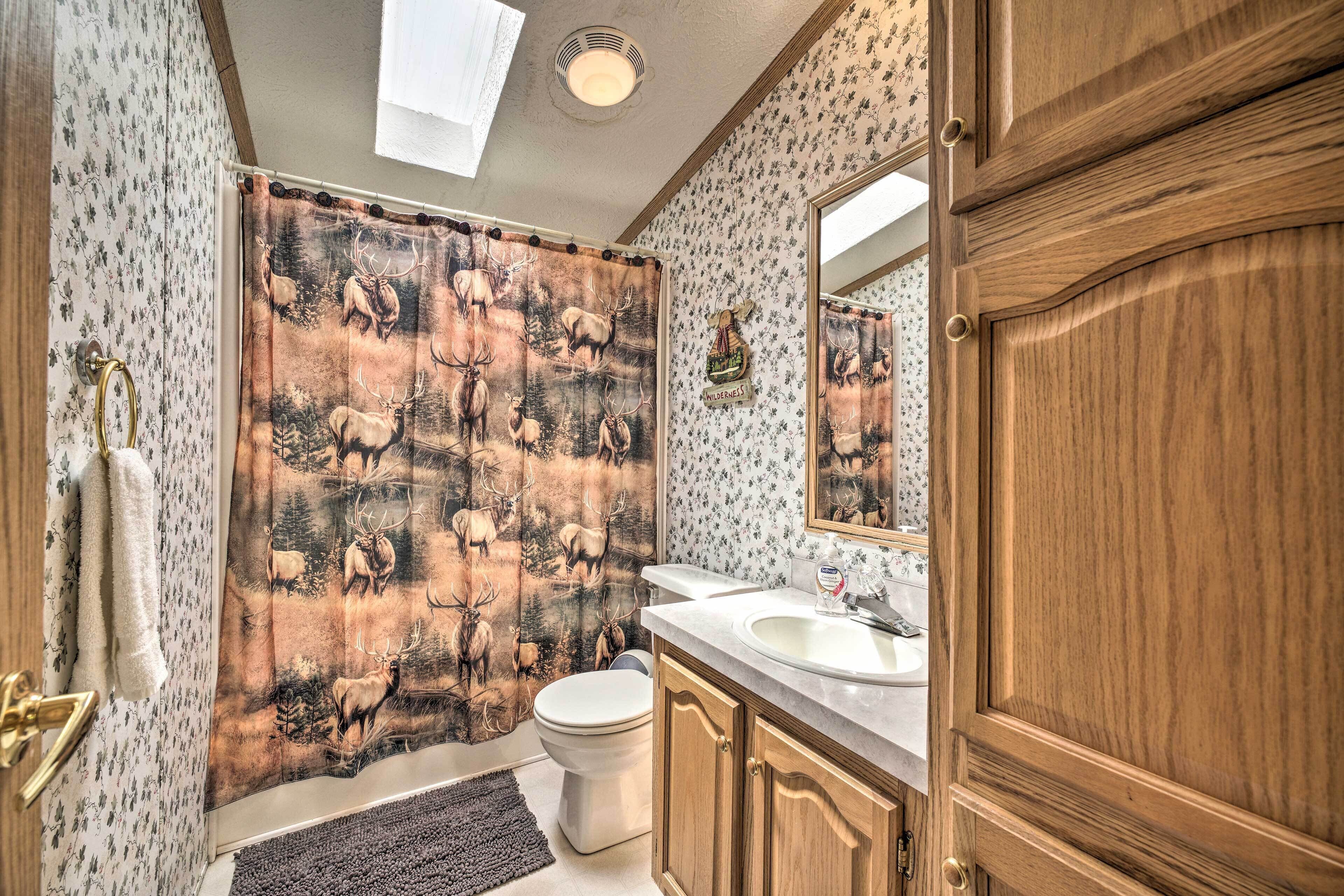 A bathroom with a shower curtain depicting elk, a toilet, a sink, and wooden cabinets.