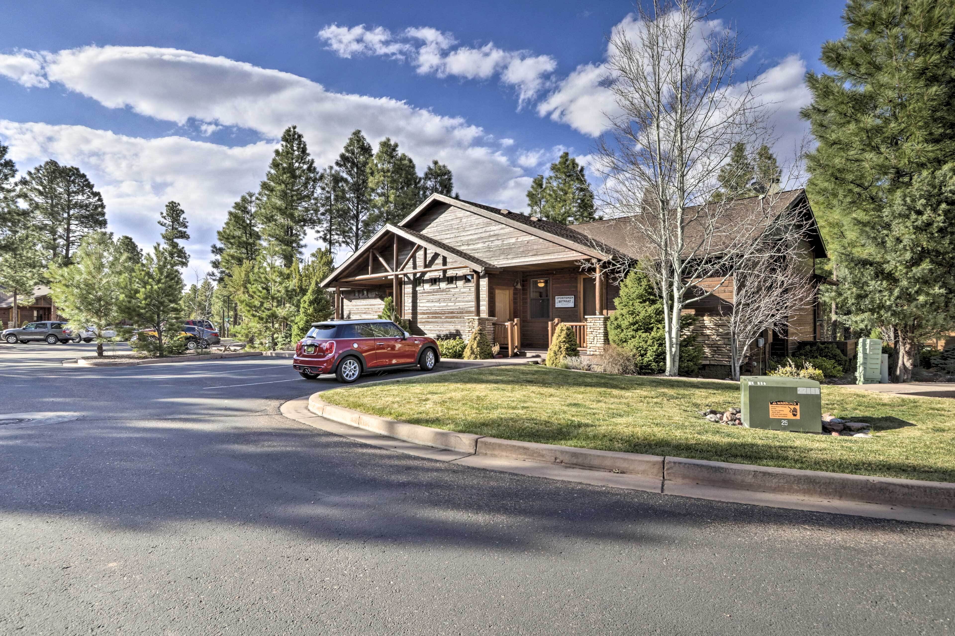 A two-story wooden cabin with a sloped roof, surrounded by a well-maintained lawn and tall pine trees.