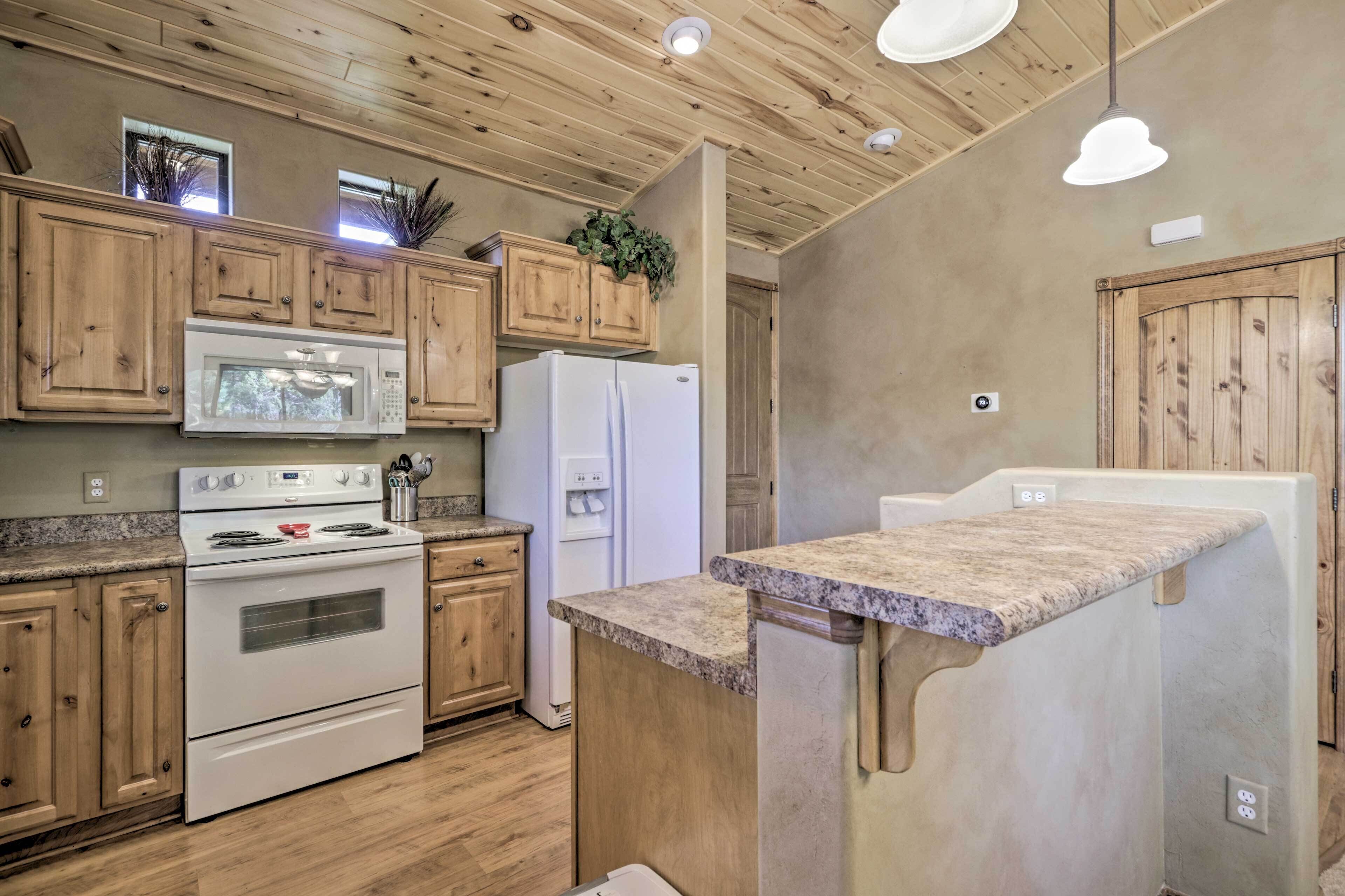 A kitchen with wooden cabinets, a microwave, a stove, a refrigerator, and a granite countertop.