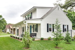 A two-story house with a covered porch, a small garden, and a black fence.