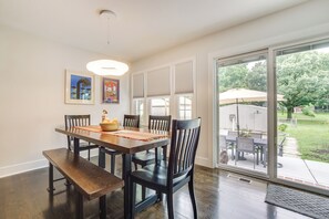 Enjoy meals in this dining area with a table, chairs, and bench, surrounded by a window with a view of the outdoor patio and framed artworks on the wall.
