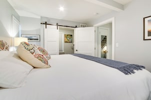 A bedroom with a large bed, a bedside table with a lamp, a door leading to a bathroom, and a staircase.