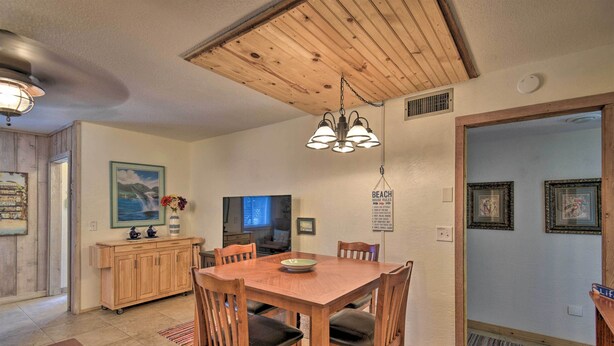 A dining area with a wooden table and chairs, a wooden ceiling, and a television in the background.